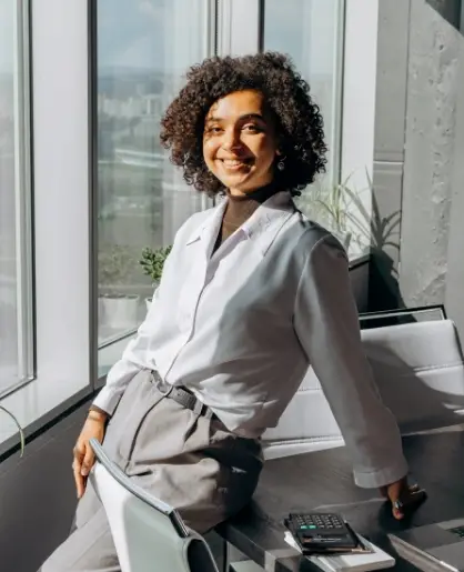 Professional woman in office attire leaning on desk in a modern workspace